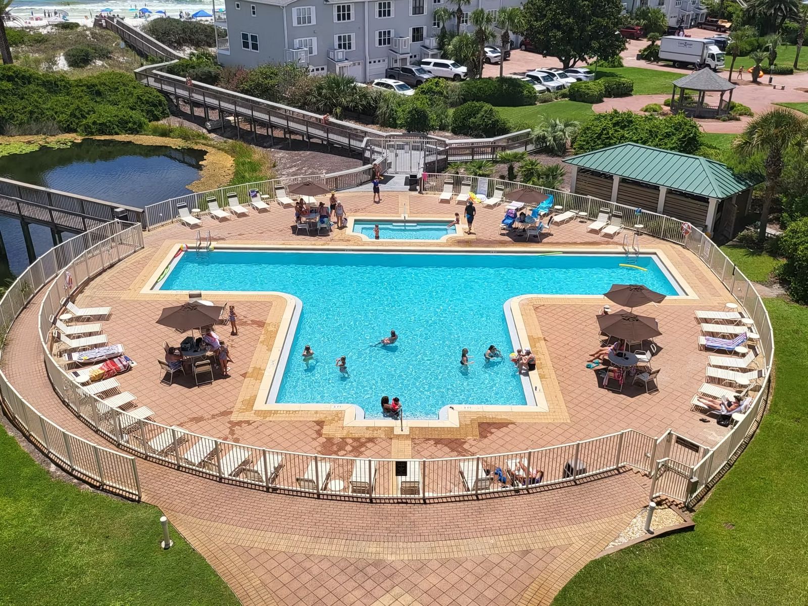 Aerial view of a condominium pool deck with pavers, fencing, umbrellas and landscaping