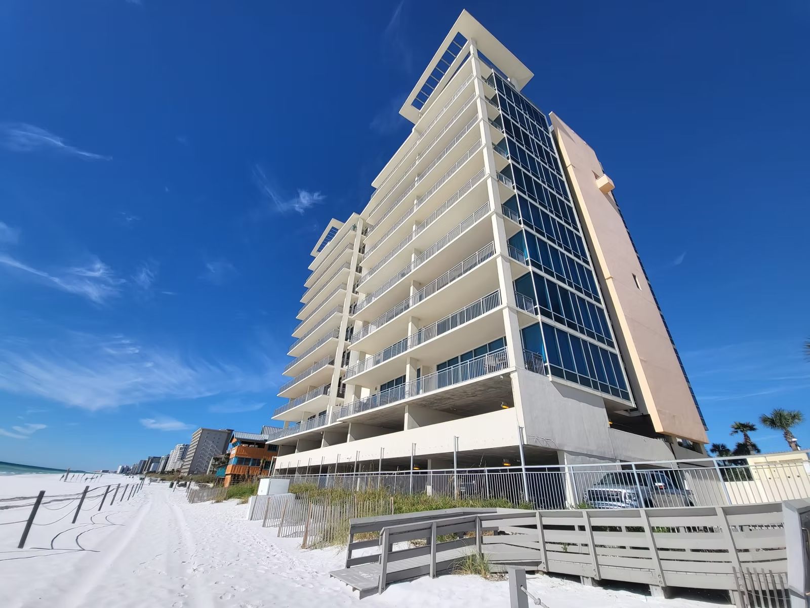 Beachfront condominium tower with stacked balconies and glass facade seen from the sand